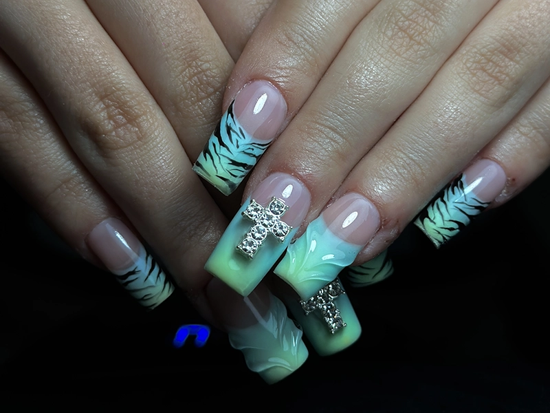 Manicura de uñas acrygel con decoraciones de una cruz de pedrería.
