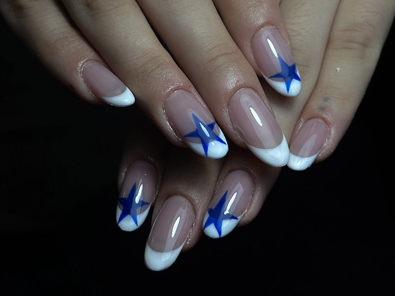 Uñas soft gel en natural combinado con blanco y con dibujo de una estrella azul en algunas uñas.